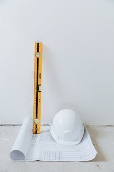 Rolled blueprint, hard hat, and level tool arranged against a white background.